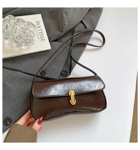 Detail of dark brown glossy baguette bag with unique wave-shaped bottom and gold metal buckle