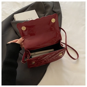 Detail of red patent leather shoulder bag with wave edge flap and gold magnetic clasp