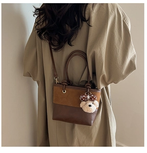 Detail of vintage brown bucket bag with plush bear charm worn over a tan trench coat