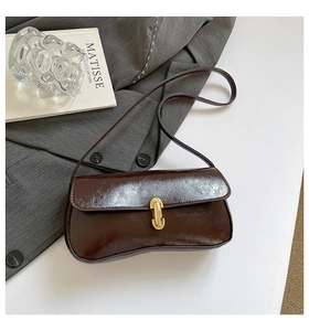 Detail of dark brown glossy baguette bag with gold buckle on elegant white display