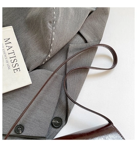 Detail of dark brown glossy leather baguette bag with slim strap on a wool blazer