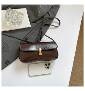 Detail of dark brown glossy baguette bag with gold buckle next to a smartphone
