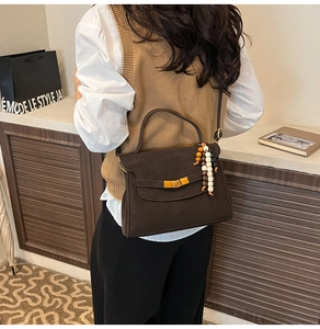 Detail of a brown leather tote bag with gold buckle and beaded tassel on a shoulder