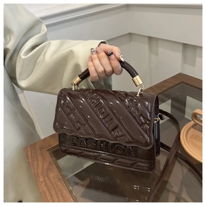 Detailed view of dark brown glossy patent leather bag with embossed fashion lettering