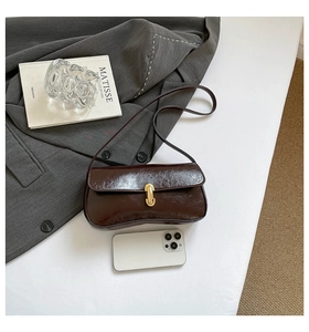 Detail view of brown baguette bag with gold buckle and leather texture next to a phone