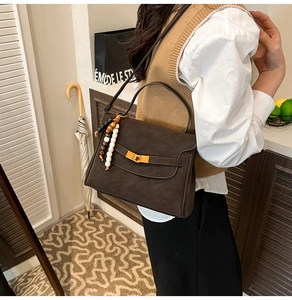 Detail view of brown tote bag featuring gold twist lock and stylish beaded tassel accessory