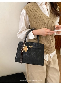 Détail d'un sac à main vintage en cuir noir avec ferrures dorées et pendentif animal