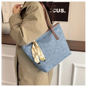 Detail of blue denim tote bag with brown leather handles and decorative silk scarf