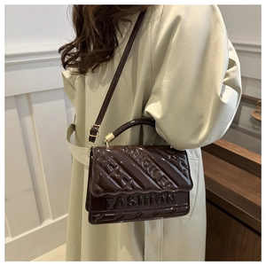 Detail of glossy dark brown patent leather shoulder bag with wide diagonal quilting