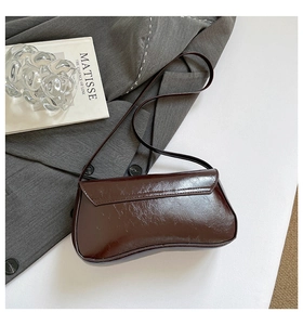 Detail of a dark brown glossy baguette bag with an asymmetric curved base and flap closure