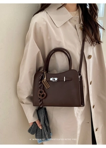 Detail of dark brown lychee leather handbag with silver twist lock and woven charm