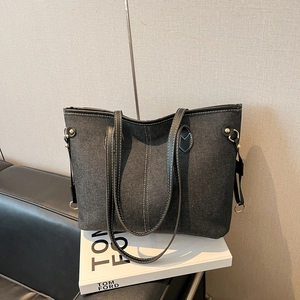 Black denim tote bag with white contrast stitching and gold hardware on white books
