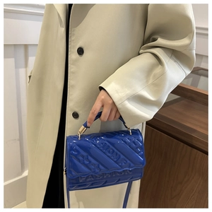 Detail of blue glossy patent leather bag with quilted fashion text and golden metal hooks