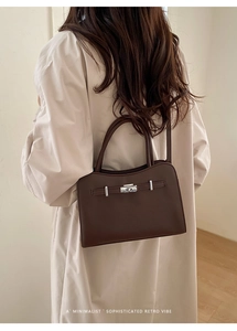 Detail of dark brown leather handbag with silver clasp on a light coat background