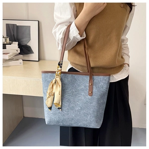 Detailed view of a blue denim tote bag with leather handles and a printed silk scarf