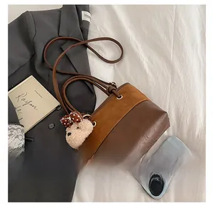 Detail of retro brown bucket bag with plush bear charm beside a smartphone case