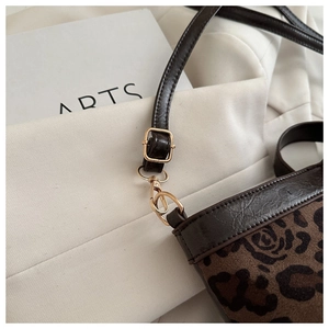 Detail of leopard print fabric with brown leather trim and golden metal strap hardware