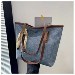 Detail of blue denim tote bag with brown leather handles and a decorative silk scarf