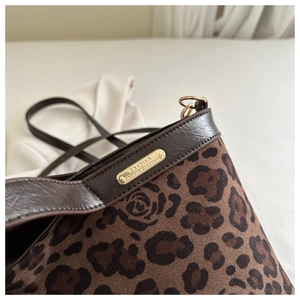 Detail of leopard print tote with rose patterns, brown leather trim, and metal plaque