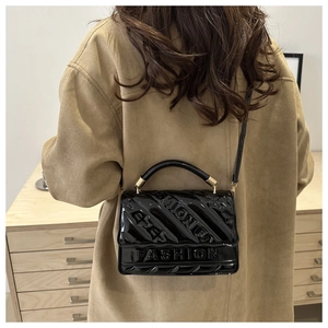 Detail of black glossy handbag with FASHION embossed logo shown on shoulder