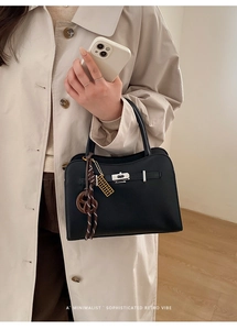 Detail of a chic black leather handbag featuring a silver lock and decorative charms