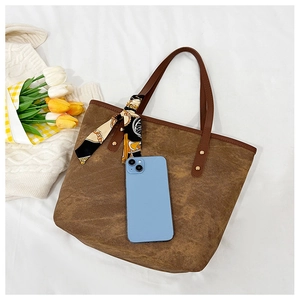 Detail of vintage canvas tote with leather handles, silk scarf, and phone for scale