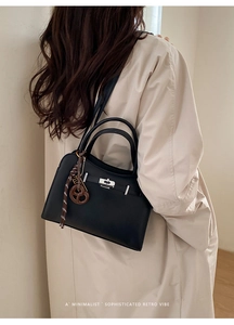 Detail of black leather handbag with silver lock and litchi texture on a model