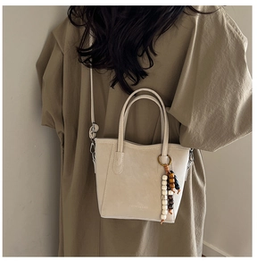 Detail of beige leather bucket bag with beaded charm and Fashion & Bags print