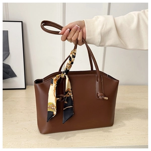 Detail of dark brown tote bag with white stitching and geometric print silk scarf handle