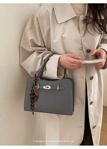 Close-up of a grey textured leather handbag featuring a silver clasp and a woven charm