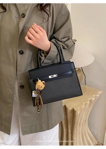 Detail of black woven handbag with leather flap and cute cat plush charm accessory