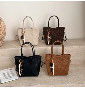 Close-up of four minimalist suede tote bags with vintage wooden bead charms on stone steps