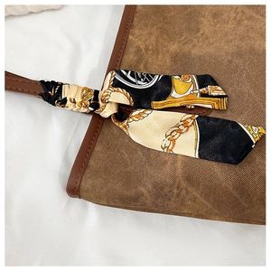 Close-up of brown canvas tote bag with leather handle and decorative silk scarf detail