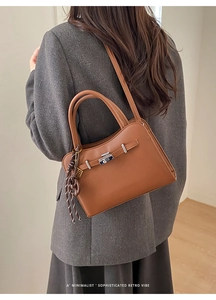Detail of a brown leather bag with silver metal twist lock and a woven lanyard charm