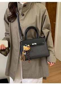 Close-up of black crossbody bag with silver twist lock and plush cat charm accessory