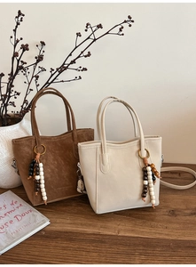 Brown suede and off-white leather tote bags with vintage beaded tassels on a wooden table