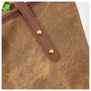 Detail of brown textured tote bag with dark leather handle and golden metal rivets