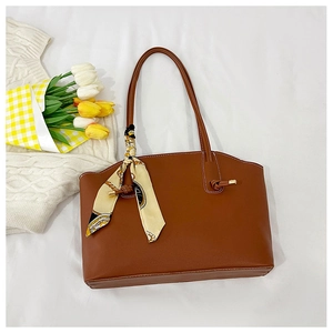 Brown faux leather tote bag with decorative silk scarf on a cozy white fabric background