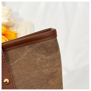 Close-up of brown canvas tote bag with leather trim, stitching details and gold studs