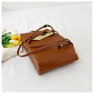 Detailed view of brown leather tote bag with white contrast stitching and silk scarf detail