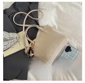 Beige bucket bag with fashion text, long strap and decorative wooden beads on white fabric