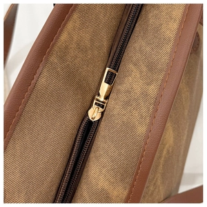 Detail of light gold metal zipper and brown lychee grain leather trim on tote bag