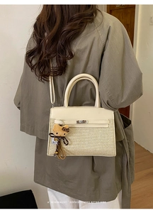 Detail of minimalist straw Kelly bag with cat plush charm shown as crossbody style