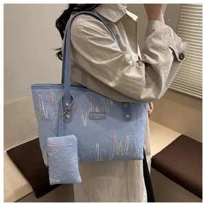 Detail of light blue tote bag set featuring rainbow wavy embroidery and metal brand plate