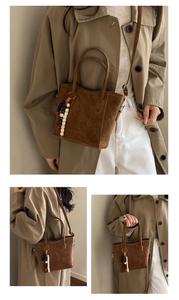 Detail view of brown matte tote bag with logo embossing and decorative bead pendant