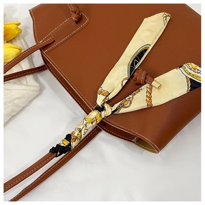 Brown leather tote bag featuring a knotted handle with a stylish patterned silk scarf detail