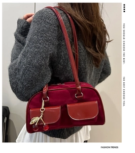 Detail of burgundy velvet shoulder bag with dual pockets and cherry charm on model