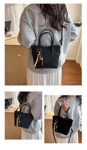 Detail of a black suede bucket bag featuring wooden bead charm and thin shoulder strap