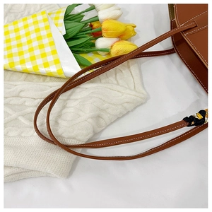 Close-up of brown leather tote bag with white contrast stitching and silk scarf detail