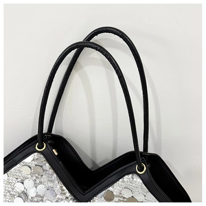 Detail of silver sequins with black leather trim and gold hardware on a tote bag
